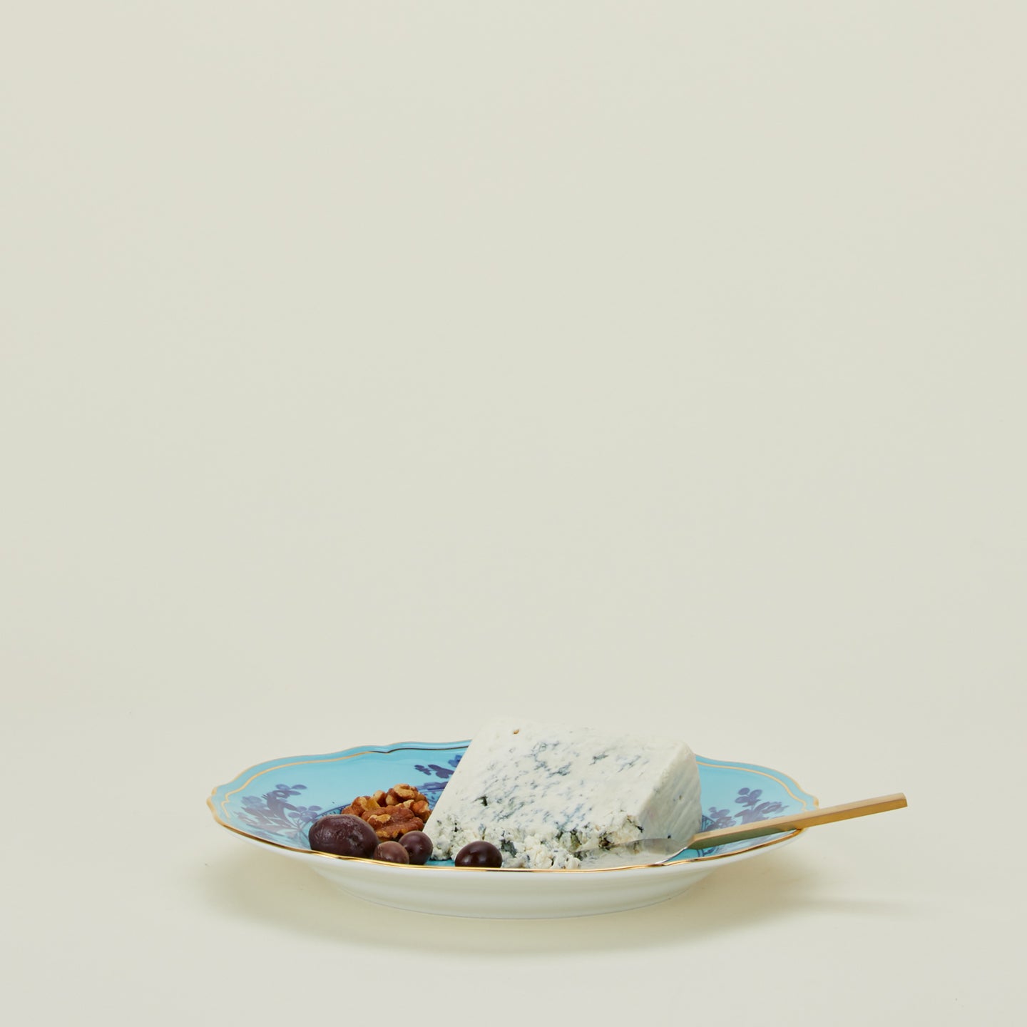 Ginori dinner plate in iris with cheese knife, cheese, and olives